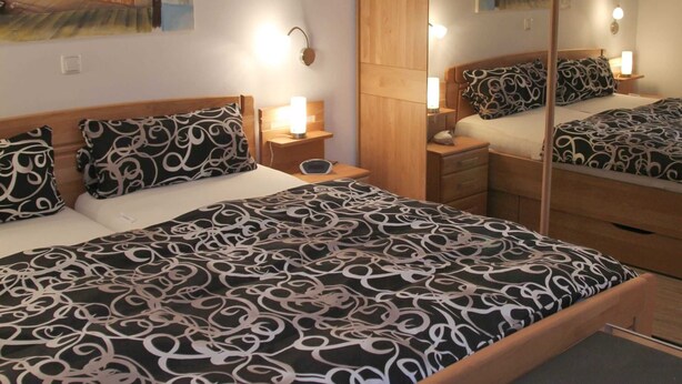 Une chambre d’hôtel avec un lit, des tables de chevet, des lampes et un grand miroir qui reflète la pièce.