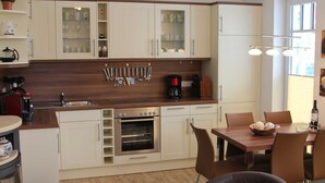 Une cuisine moderne avec des meubles blancs, un plan de travail en bois et un coin repas comprenant une table et des chaises.