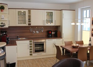 A modern kitchen with white cabinets, a wooden countertop, and a dining area with a table and chairs. - Meeresbrise Fireplace · Patio · 250 m to the beach - Meeresbrise Accommodation (Börgerende-Rethwisch)