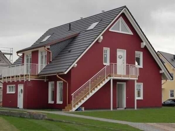 A red two-story house with a balcony, a staircase, and a garage.