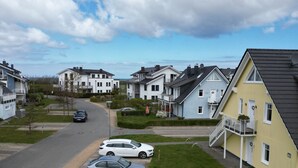 Une rue résidentielle bordée de maisons, avec un ciel dégagé et des voitures garées.