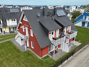 A red two-story house with a balcony, a small patio, and a fenced yard.