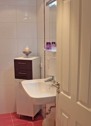 A bathroom with a white sink, a mirror, a cabinet with drawers, and a small shelf with purple containers.