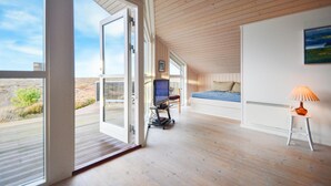 Een moderne slaapkamer met een groot schuifglas dat uitkomt op een buitenruimte, een bed, een bureau met een computer en een kleine tafel met een lamp.