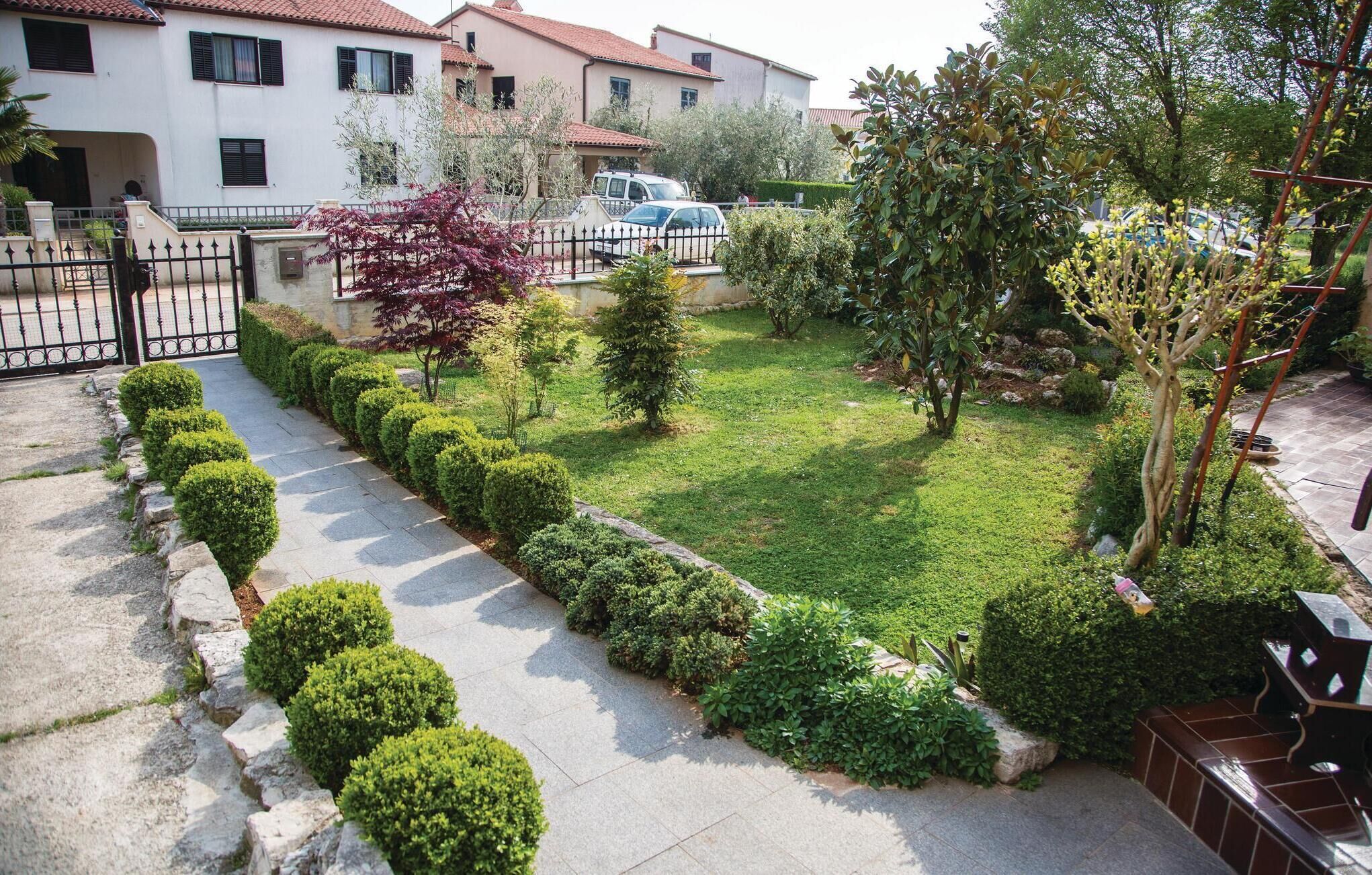 Un jardin bien entretenu, avec un chemin pavé, des arbustes taillés avec soin et une variété d’arbres.