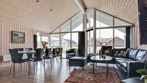 Uma sala de estar espaçosa com uma janela grande, uma área de jantar com cadeiras, um sofá e uma mesa de centro.