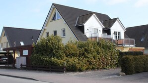 A row of two-story houses with sloped roofs, a covered parking area, and a well-maintained hedge.