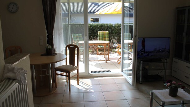 A living room with a TV, a dining table, chairs, a potted plant, and a sliding glass door leading to an outdoor patio.