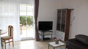A living room with a TV, a glass coffee table, a sofa, a cabinet with glass doors, and a dining area with a chair and table.