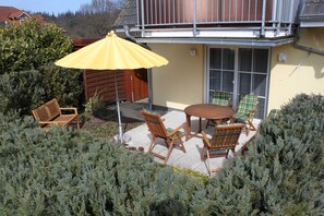 An outdoor patio with a wooden table and chairs, a yellow umbrella, and a wooden bench. - Apartment Sanddorn - Apartment Sanddorn-1 bedroom for max. 4 persons and 1 baby (Karlshagen)