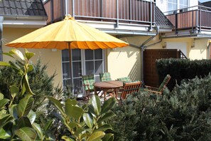 Um pátio com um guarda-sol amarelo, móveis de madeira e plantas verdes.