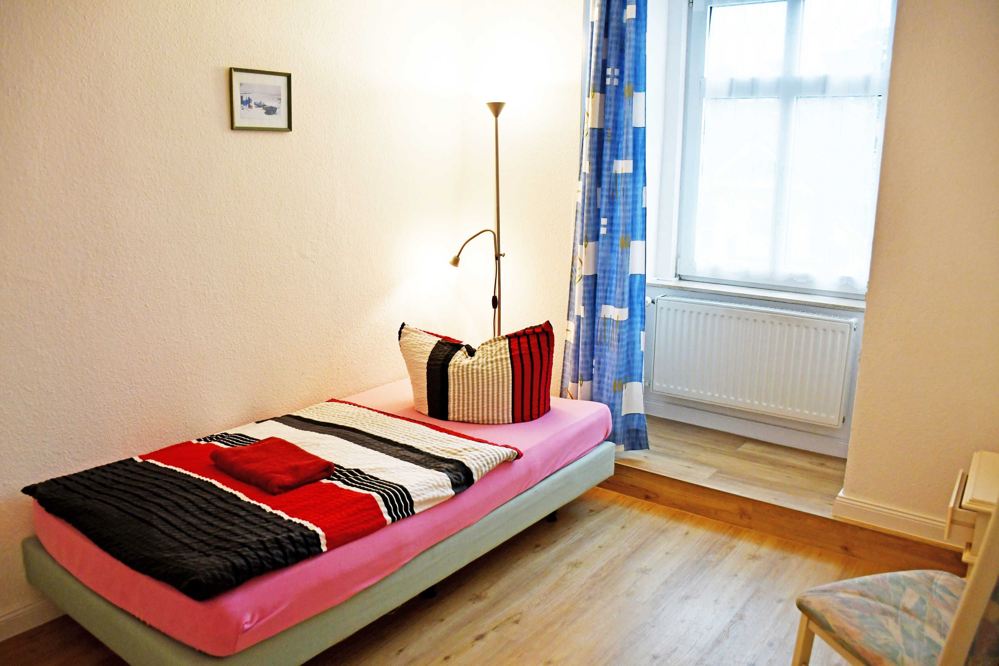 A single bed with a pink mattress, a bedside lamp, and a window with blue curtains.