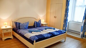 A bedroom with a wooden bed, two bedside tables, a wardrobe, and a window with curtains. - Shared rooms (2-room-A) - Villa in Baabe (Baabe)