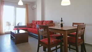 A modern living room with a red sofa, wooden dining table, and chairs. There is a small coffee table, a potted plant, and a bottle of wine on the table. - Amazing apartment in Roldán with swimming pool (Roldán)