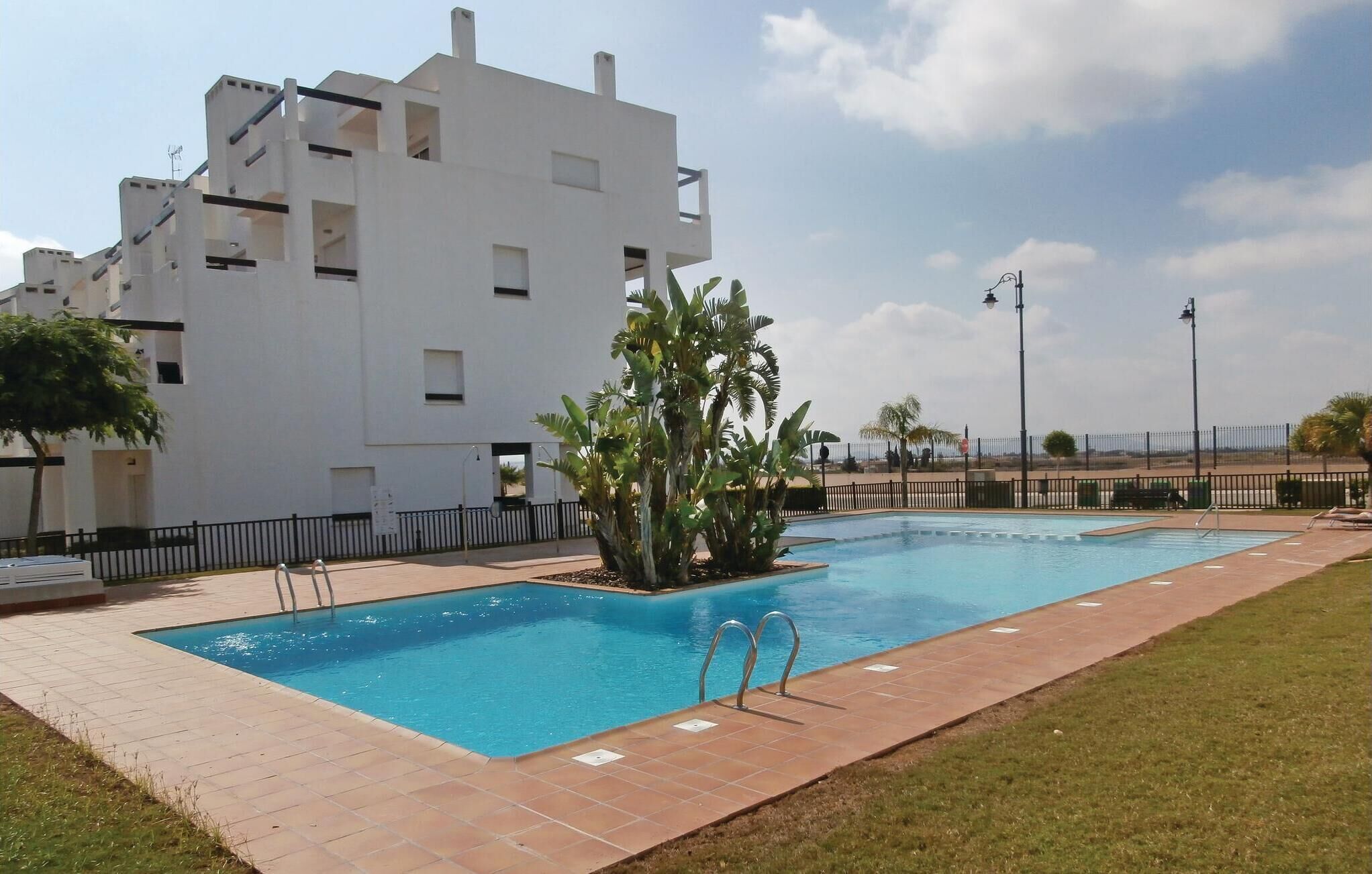 Un bâtiment moderne doté d’une piscine, entouré d’une clôture et de palmiers.