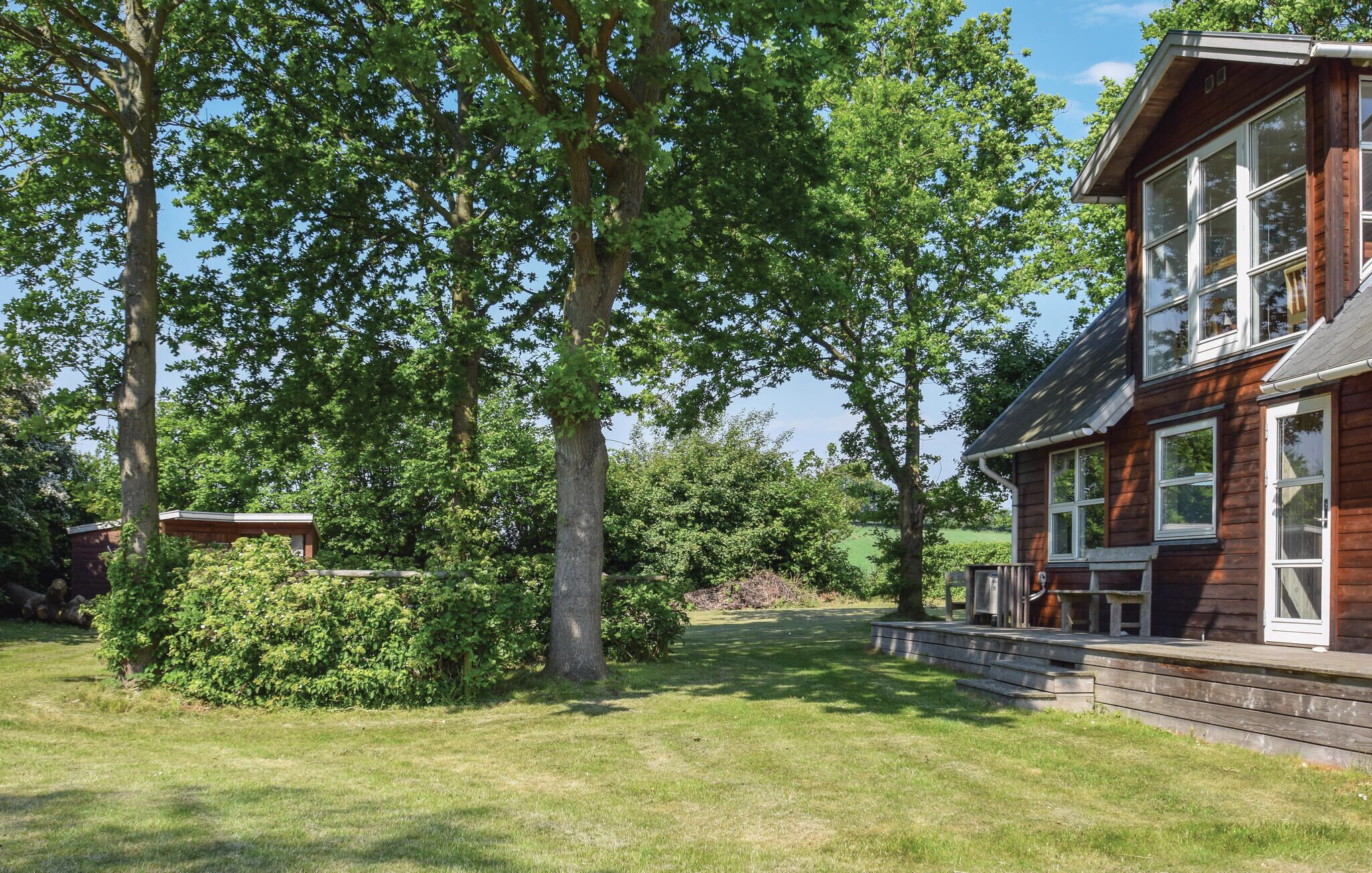 A two-story wooden house with a large front porch, surrounded by lush green trees and a well-maintained lawn.