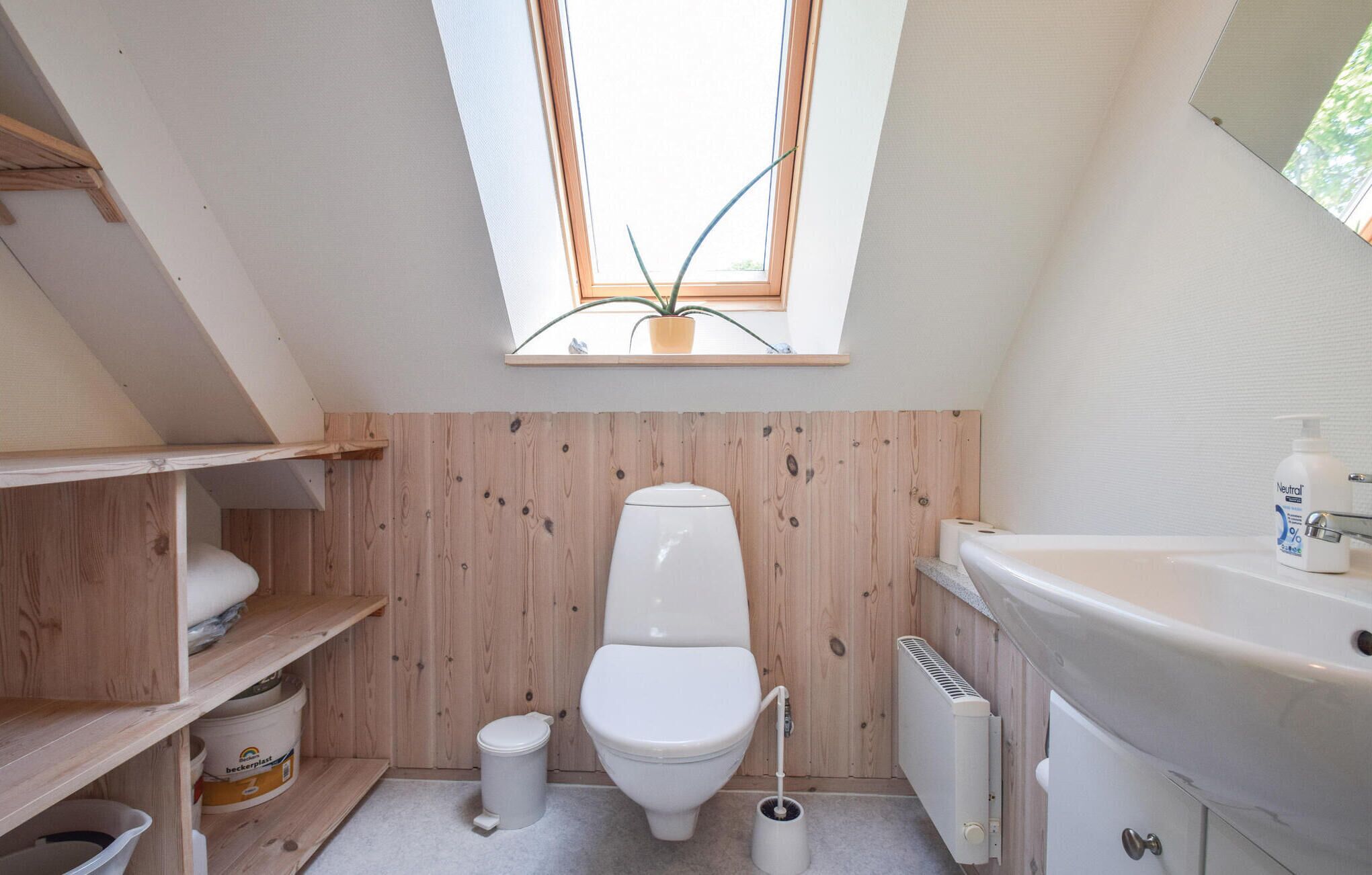 A small, compact bathroom with a skylight, wooden walls, a white toilet, a radiator, and a shelf with storage bins.