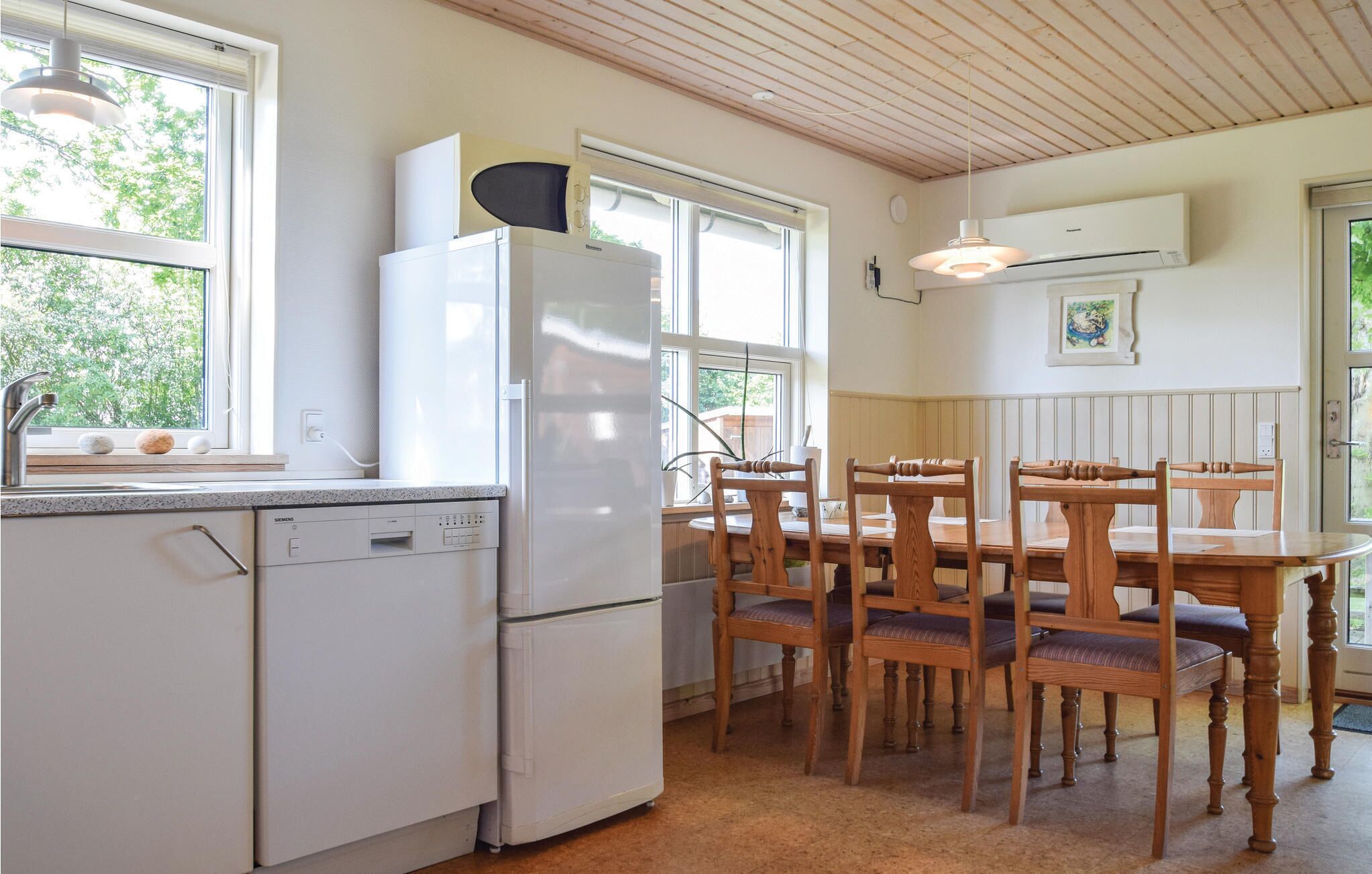 Ett kök med vita vitvaror, en matplats med trästolar och stora fönster.