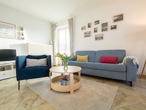 Un soggiorno con un divano blu, un tavolino rotondo in legno, una TV e un termosifone.
