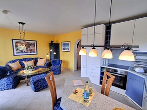 A living room with a sofa, chairs, a dining table, and a kitchen area with cabinets and appliances.