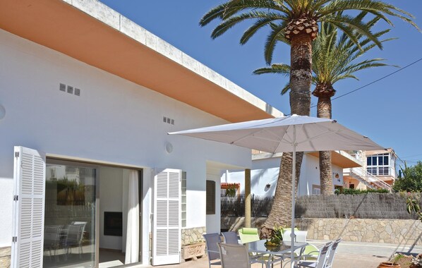 Ein modernes Gebäude mit weißer Fassade, einer überdachten Terrasse mit Gartenmöbeln und einer Palme.
