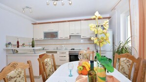 A dining area with a table set for two, a kitchen in the background, and a potted orchid on the table. - Amazing apartment in Omis with WiFi (Omis)