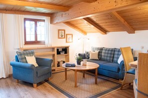 Un salon chaleureux avec un canapé bleu, un fauteuil bleu, une table basse en bois et une bibliothèque.