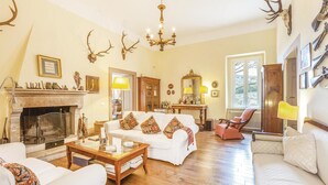 A traditional living room with a fireplace, white sofas, patterned cushions, and antler decorations.