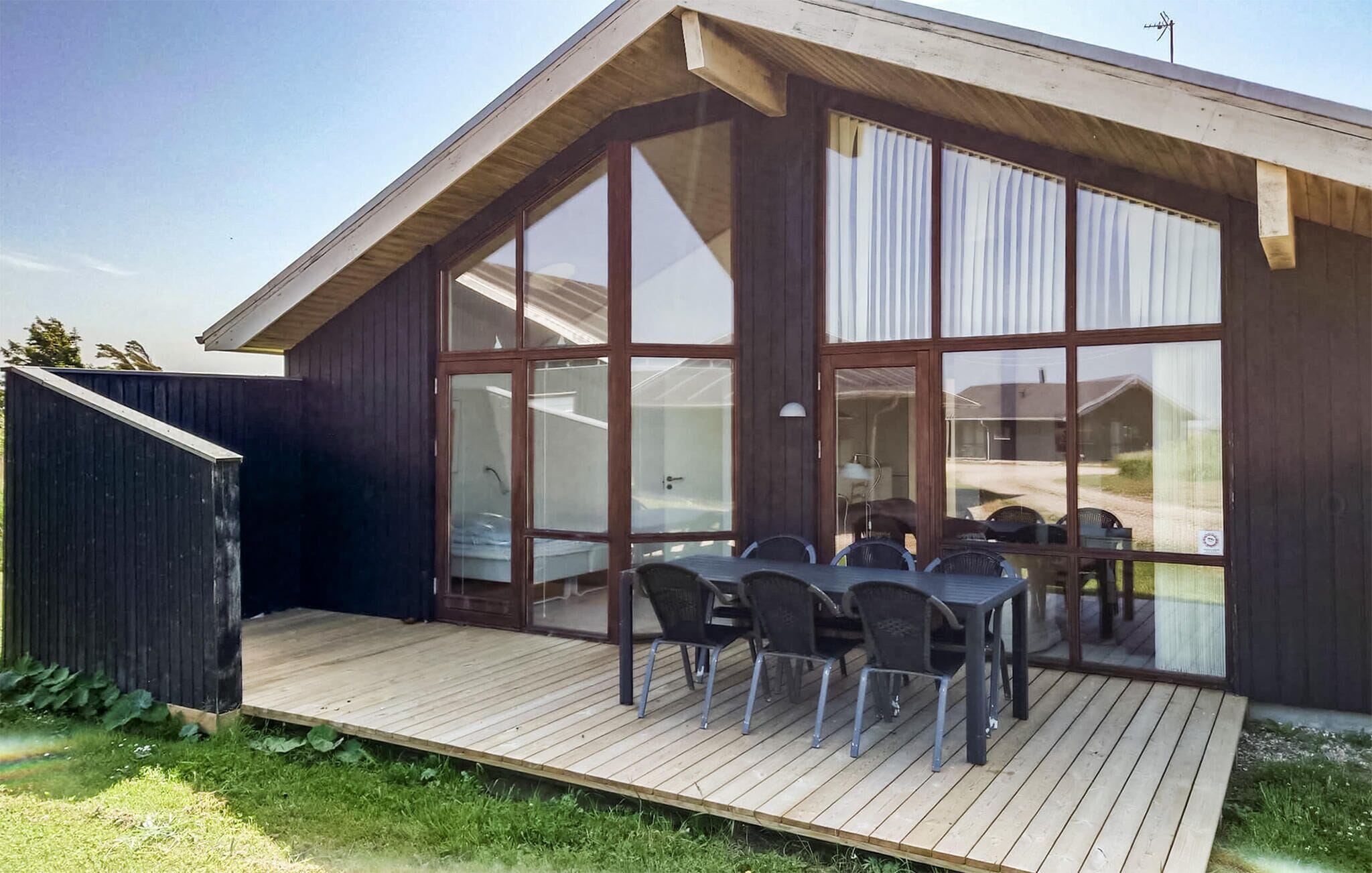 Ein modernes Gebäude mit einer Holterrasse und einem gläsernen Patio-Bereich mit Sitzgelegenheiten im Freien.