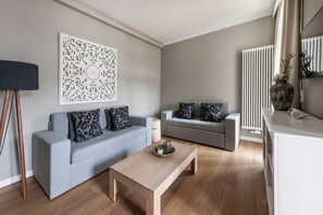 Uma sala de estar moderna com dois sofás cinza, uma mesa de centro de madeira, um painel branco decorativo e um radiador.