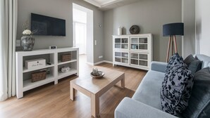 Ein Wohnzimmer mit grauem Sofa, einem Couchtisch, einem weißen Schrank, einem Fernseher und einer Stehlampe.