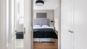 Ein Schlafzimmer mit einem Bett, einem Nachttisch, einer Wandleuchte und einer Tür zu einem anderen Raum.