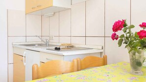 Una pequeña cocina con un fregadero, estufa y una mesa cubierta con mantel floreado.