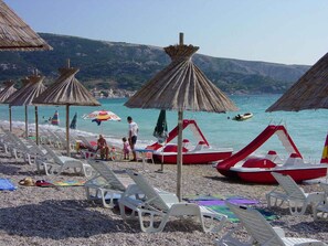 A beach with rows of white lounge chairs, thatched umbrellas, and a red boat.