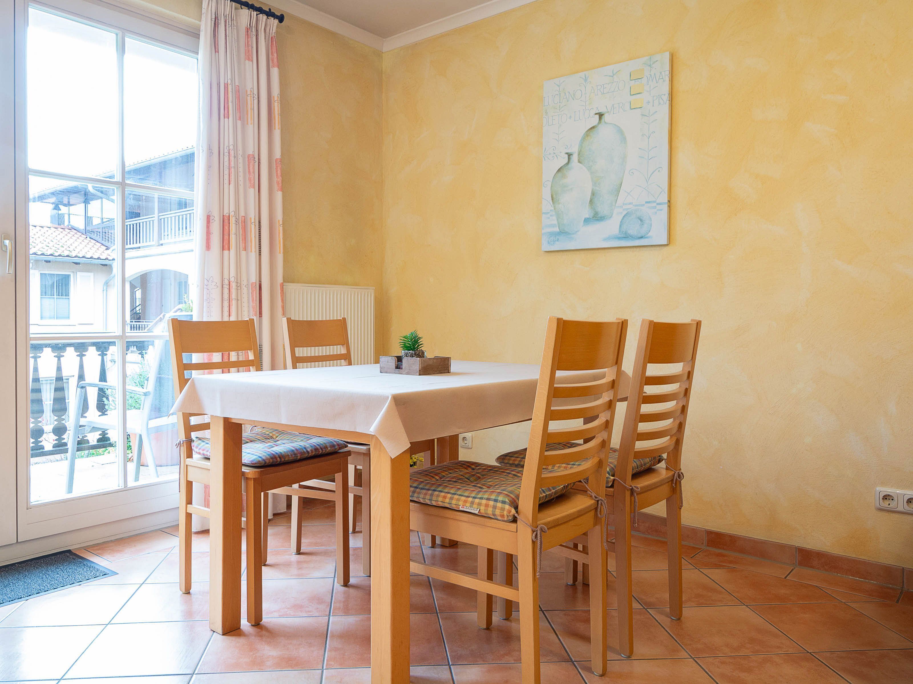 A dining area with a table and chairs, a potted plant, and a painting on the wall.