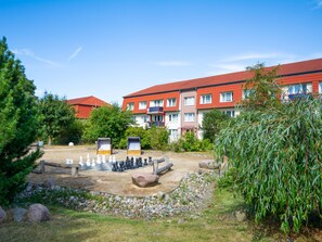 A courtyard with a chessboard, surrounded by trees and a building with red roofs.