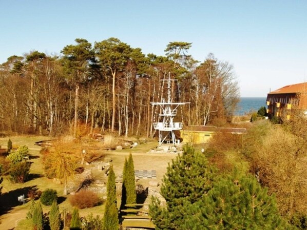 A coastal area with a tall white structure, possibly a lighthouse, surrounded by trees and a building with a red roof.