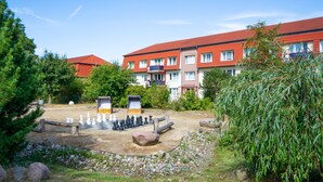 A courtyard with a chessboard, surrounded by trees and a building with red roofs. - Dune garden Whg. Wa47-24 - Wa47-24 (Kühlungsborn)