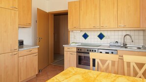 A compact kitchen with wooden cabinets, a stove, and a sink. - Dune garden Whg. Wa47-24 - Wa47-24 (Kühlungsborn)
