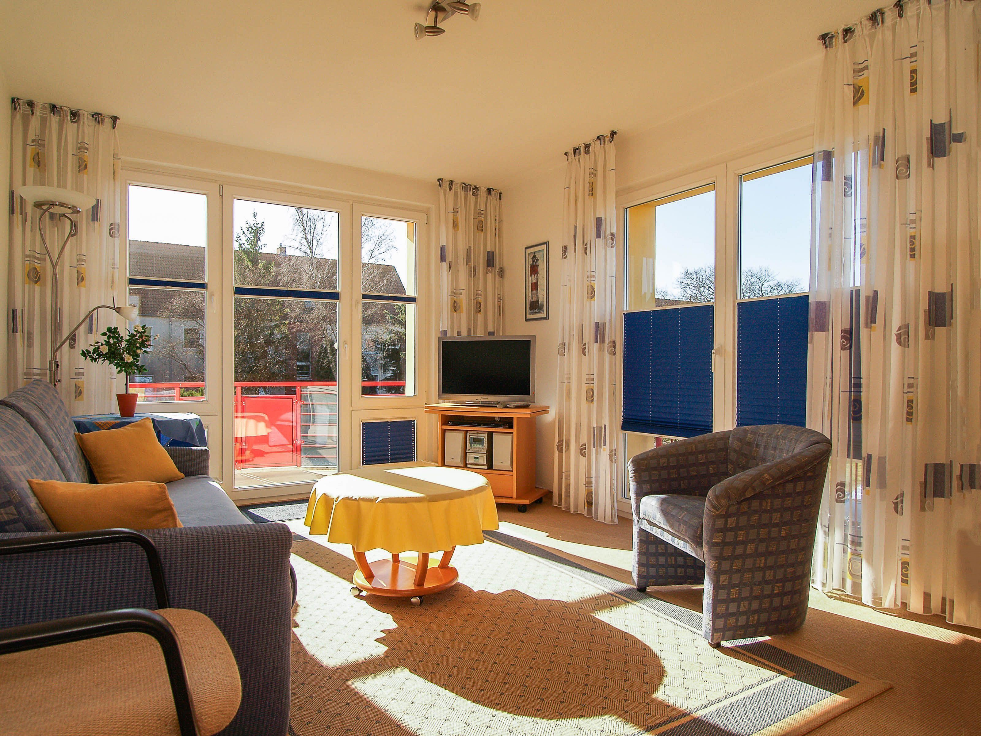 A living room with a sofa, armchair, TV, and a table with a yellow tablecloth.