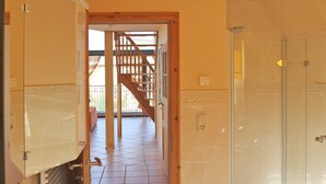 Un baño con ducha de vidrio, piso de cerámica y una escalera de madera que lleva a un área exterior.