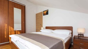 A neatly made bed with a wooden headboard, a bedside table with a lamp, and a wardrobe with a mirror.