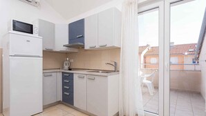 A compact kitchen with a refrigerator, microwave, and sink. It features a sliding glass door leading to a balcony with a view of buildings.
