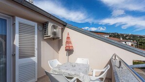 A balcony with a table and chairs, an air conditioning unit, and a red and white striped umbrella.