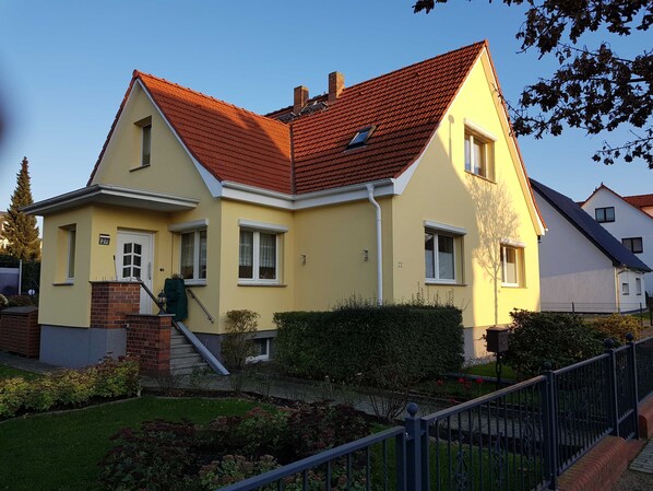 A two-story house with a red-tiled roof, a front entrance with a door, and a small window on the upper floor.