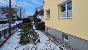 A residential building with a yellow facade, a paved pathway, and a snow-covered ground.