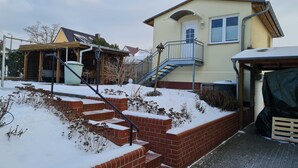 A two-story house with a brick staircase leading to a balcony, a covered porch, and a garage.