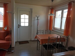 Une pièce comprenant une table à manger, des chaises, un canapé, une lampe sur pied, un porte-manteau et une porte avec une fenêtre.