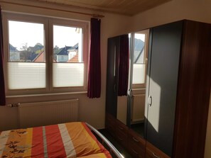 Ein Schlafzimmer mit Bett, Schrank, Heizkörper und einem Fenster mit Vorhängen.