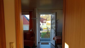 A hallway leading to a balcony with a red chair, a table, and a door.